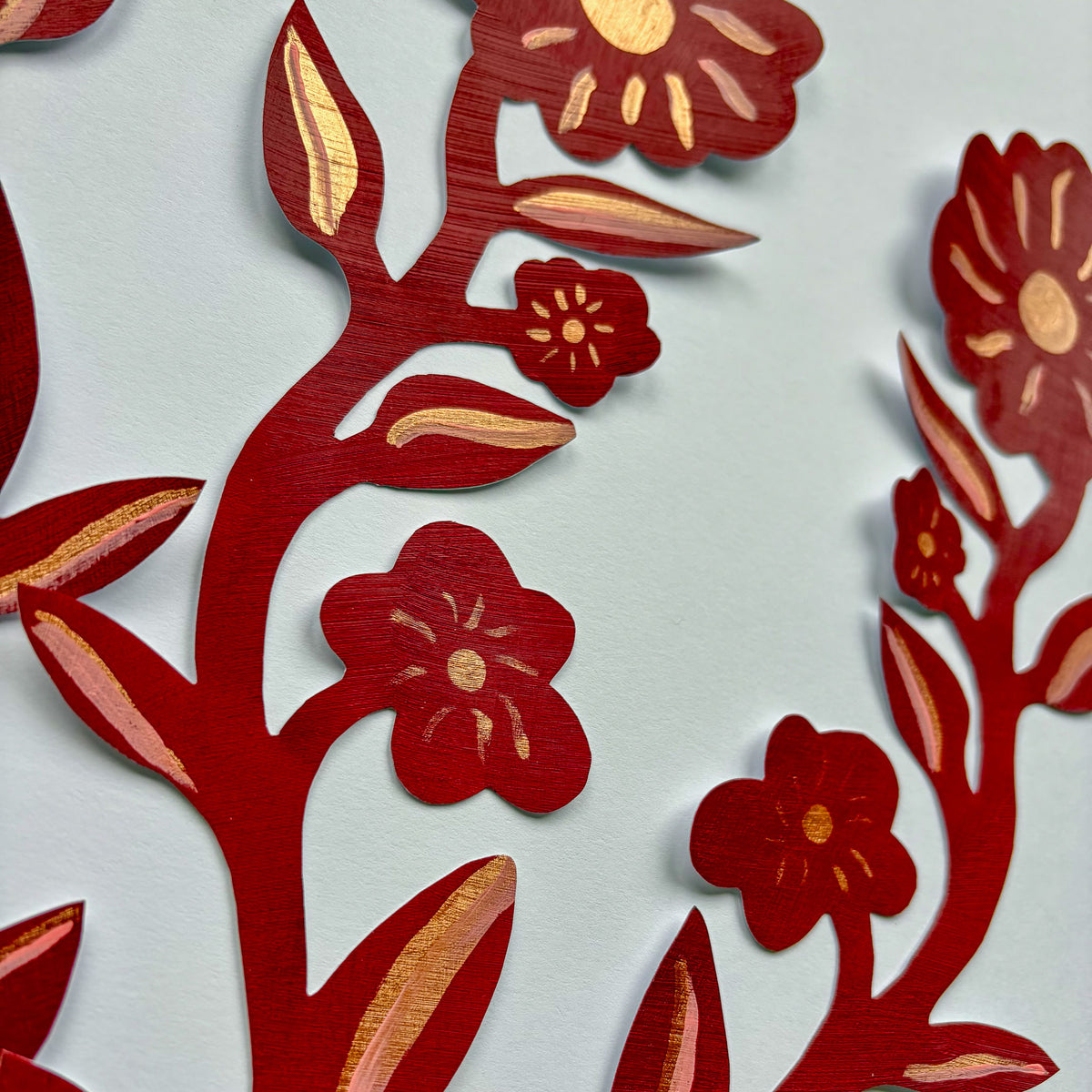 Nærbillede af de håndmalede detaljer og de gyldne accenter på en rød blomster wall sticker