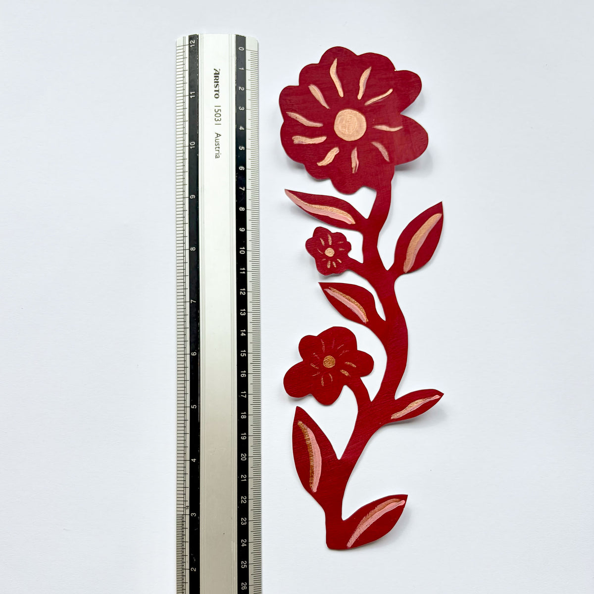 Håndmalet blomsterranke med tre blomster lagt ved siden af en lineal som størrelsesreference